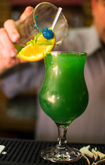 Bartender making refreshing coctail on a bar background. Dark moody style. Ice in tha glass