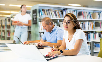 Obraz premium Female Latina college student working on a project with a male elder in the school library