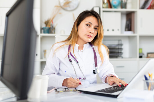 Young hispanic woman doctor assistant working in medical office using laptop computer