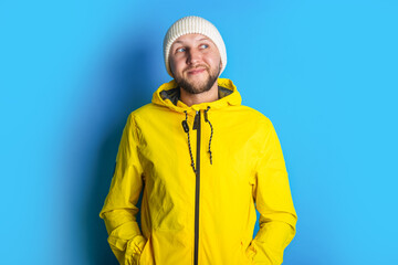 A pensive young man in a yellow jacket looks to the side against a blue background