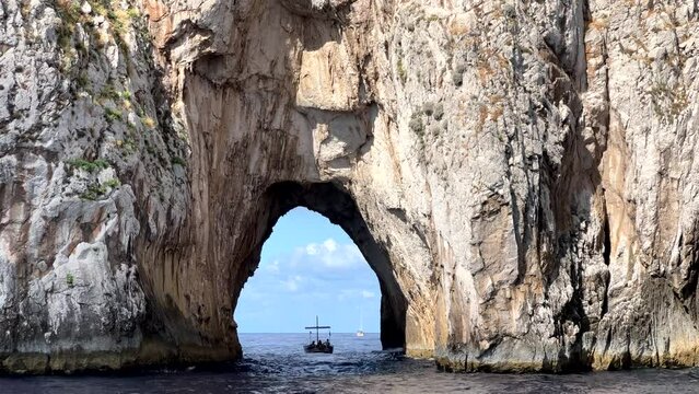 Boat passing trough the arch of Faraglioni rock by Capri island in Italy
