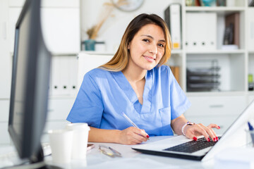 Portrait of young latina female doctor working on laptop in clinic office