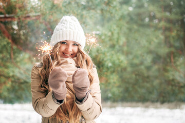 Beautiful sweet girl holds sparklers in her hands. Girl is blonde against the background of the winter forest. Concept of the holiday - New Year, Christmas, St. Nicholas Day. Banner. Place for text.