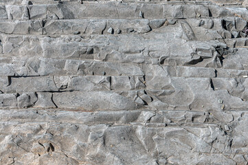 Stone wall is gray with different sand colored spots and different bulges. Textured stone background is gray with pale patterns.
