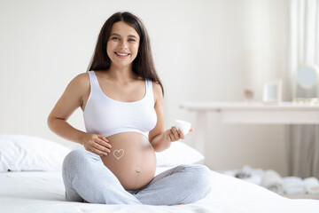 Cheerful attractive pregnant woman massaging her big belly, using cream