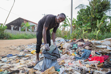 Young african man looks at the camera while collecting waste from the ground