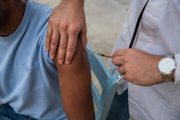 A seated black patient taking his jab from a caucasian general practitioner