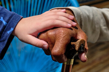 Grandfather and grandson holding hands. Mixed race family. Dark skin toned grandfather with light skin toned grandchild. Grandchild holding grandparent's hand. Grandfather leaning on a walking stick.