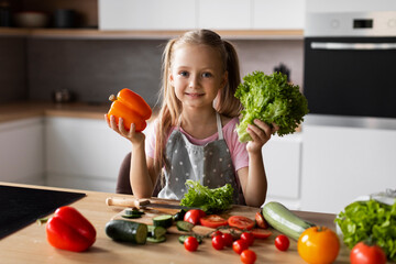 Happy pretty caucasian little girl holding organic vegetables for salad in modern kitchen interior