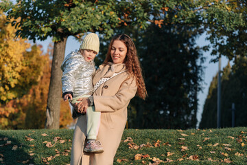 Smiling Caucasian Mother Holding Daughter. Laughing In The Park, Fall Season. Happy loving family. Mother and her child walking outdoor.