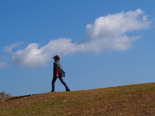 青空と白い雲をバックに歩く高齢日本人女性