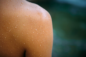 Close-up female tanned shoulder, showing skin detail with water droplets and goose bumps. Part of young sexy woman body. Blurred background, copy space.