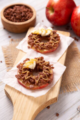 Creative party snack for holidays. Apple rounds with peanut butter, caramel and chocolate flavor puffed rice topping with banana slices. Funny appetizer for kids and adults.