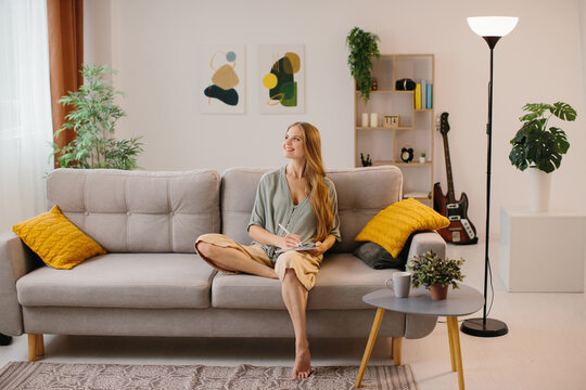 Happy young designer drawing on a graphics tablet with a stylus pen. Female graphic designer smiling while working on a new design. Creative young freelancer working in her home office.