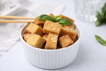 Bowl with delicious fried tofu, basil and sesame seeds on white table