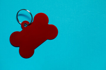 Red pet tag in shape of bone with ring on light blue background, top view. Space for text
