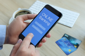 Man using online banking app on smartphone at wooden office table, closeup