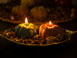 Pumpkin shape candles in a cozy arrangement. Warm light of the glowing soy wax illuminates the decoration. Stylish seasonal objects for the autumn mood.