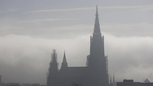Time lapse shot with the silhouette of the Ulm minster in front of low clouds and fog under a blue sky at a morning in autumn