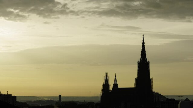 Time lapse shot with the silhouette of the Ulm minster in front of a yellow sky at morning with some clouds