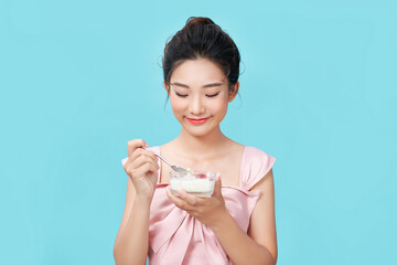 Young woman eating yogurt on blue background