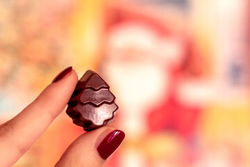 Advent chocolate Christmas tree, girl holding a festive praline, yellow bokeh bg