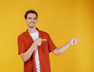 Portrait of young man pointing fingers at copy space isolated on yellow studio background