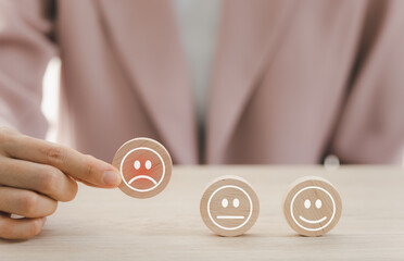 closeup businesswoman hand picking bad emotion face on round wooden piece arranged on table for satisfaction survey