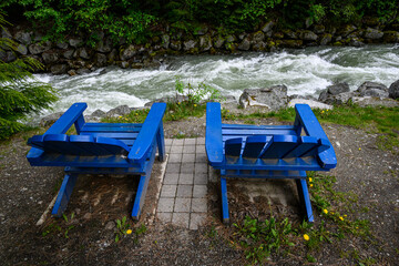 Bright blue Adirondack chairs on the bank of Fitzsimmons Creek, Whistler, BC, Canada
