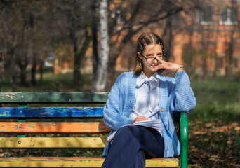 A teenager on a bench is doing homework on a sunny autumn day.