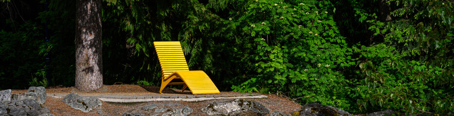 Bright yellow chaise lounge outdoors in a sun beam on a patio in the woods
