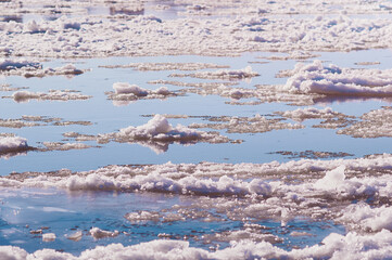 Ice floes float on the river. Seasonal ice drift. Reflection of the blue sky in the water. Natural...