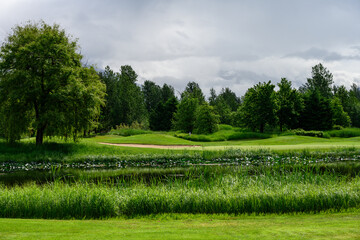 Water hazard and sand trap on a lush green golf course, stormy clouds in background
