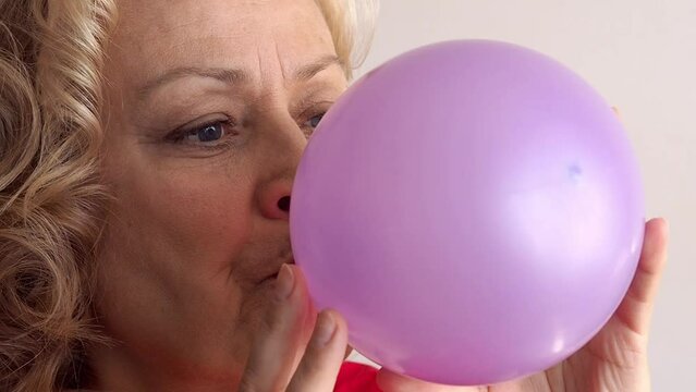 Close-up of a mature woman inflates a balloon. Birthday celebration preparation concept