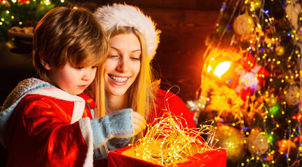 Fototapeta na wymiar Mother and son in Santa costume opening Christmas amazing gifts. Family winter holidays and people concept.