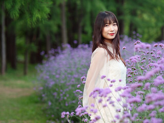 Beautiful woman in white dress standing in purple Verbena Bonariensis flower field, charming Chinese girl with black long hair enjoy her leisure time outdoor.