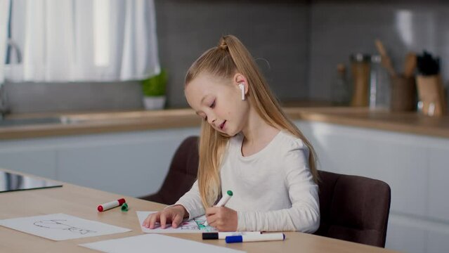 Modern kids leisure. Carefree little girl drawing picture at kitchen and listening to music via earbuds, empty space