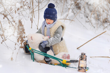 The boy is taking his teddy bear on a sledge to visit Santa Claus. he's going to celebrate the new year.