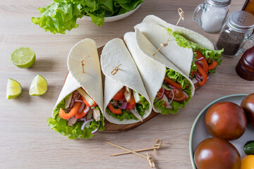 chopped fresh vegetables and chicken fillets wrapped in homemade tortillas lie on a wooden board....