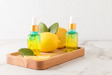 two cosmetic bottles with a colored glass pipette with a natural lemon remedy on a wooden tray with lemon fruit and leaves.