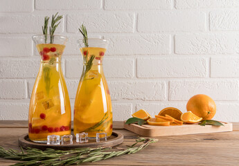 two decanters for water with a cold refreshing drink of orange and berries, with sprigs of rosemary...