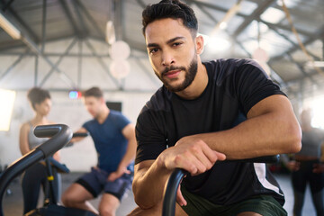 Gym, portrait and man exercise on spinning bike for health, training and fitness goal at a sports center. Personal trainer, coach and mexican man with a vision for wellness, heart health and workout