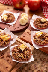 Creative party snack for holidays. Apple rounds with peanut butter, caramel and chocolate flavor puffed rice topping with banana slices. Funny appetizer for kids and adults.