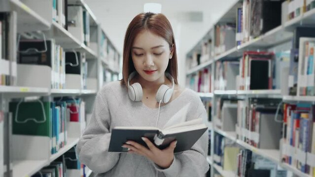 Asian young student girl in sweater reading the book from bookshelf in university or college library.