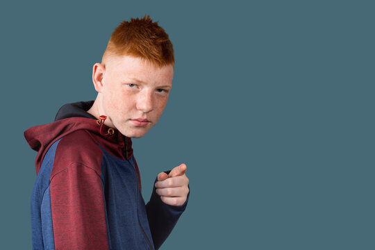 A teenager, a boy with red hair, wearing a hoodie shakes his finger.