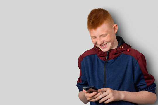 A teenager with red hair communicates on social networks using a smartphone, with a joyful expression on his face