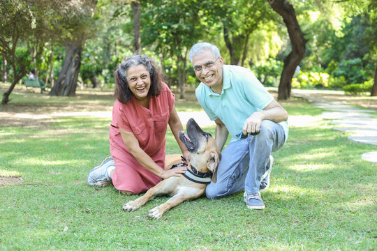 Happy Indian Senior Couple Playing With Dog In Summer Park. Retirement Life, Retired People Enjoying Life In Garden. Having Fun.