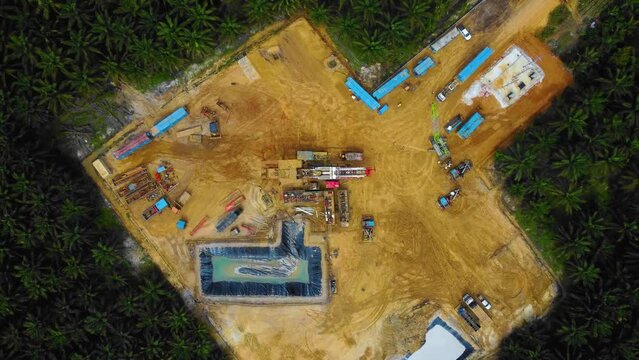 Cinematic Drone Footage of Onshore Drilling Rig equipment structure for oil exploration and exploitation in the middle of jungle surrounded by palm oil trees during sunset and high oil price.