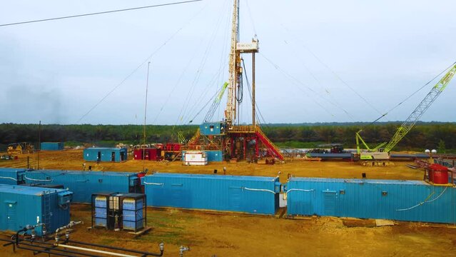 Cinematic Drone Footage of Onshore Drilling Rig equipment structure for oil exploration and exploitation in the middle of jungle surrounded by palm oil trees during sunset and high oil price.