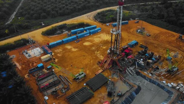 Cinematic Drone Footage of Onshore Drilling Rig equipment structure for oil exploration and exploitation in the middle of jungle surrounded by palm oil trees during sunset and high oil price.